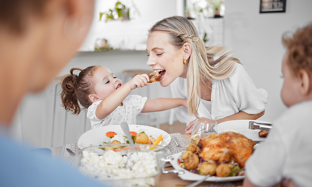 Happy family, mother and child eating chicken and vegetables in a healthy meal for dinner in Germany, Berlin. Food, nutrition and young girl feeding her hungry mom lunch at a home dining room table